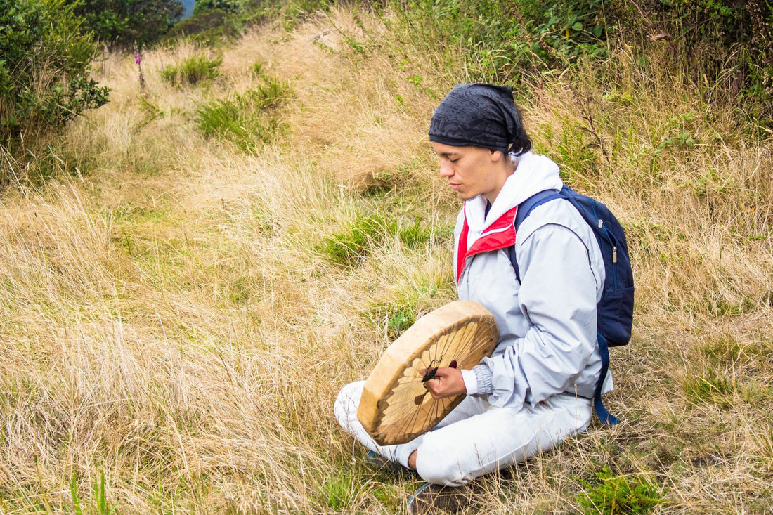 Femme hispanique assise par terre sur l'herbe et jouant sur un tambour de chaman